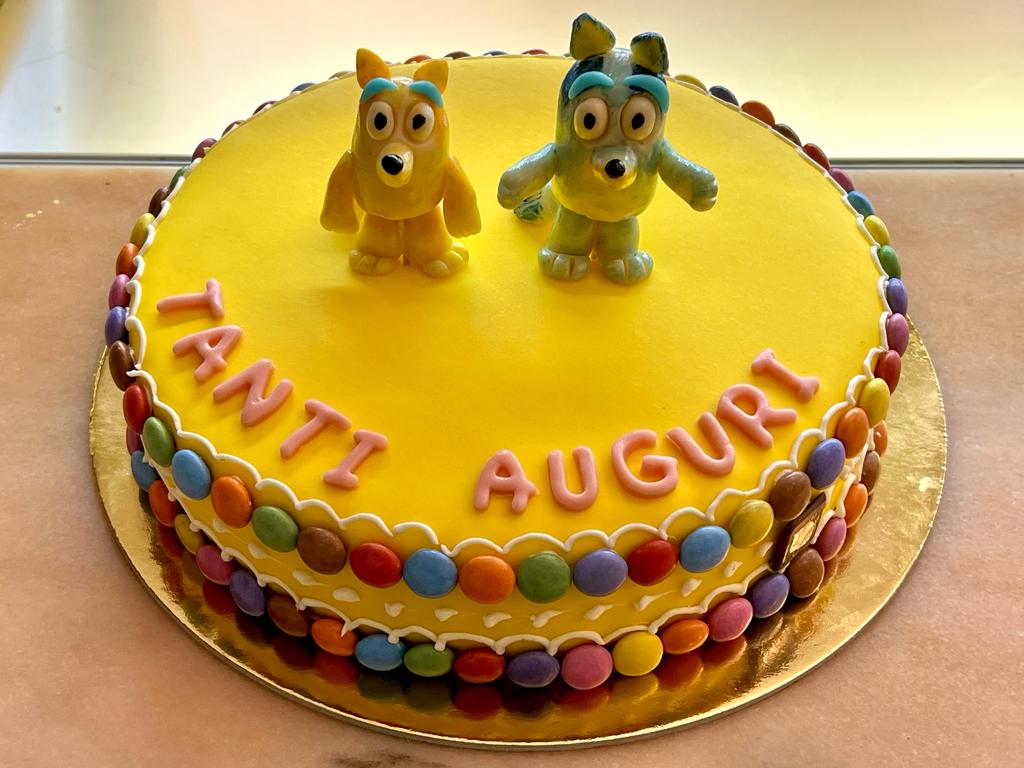 Torta gialla con statuine e scritta di auguri
