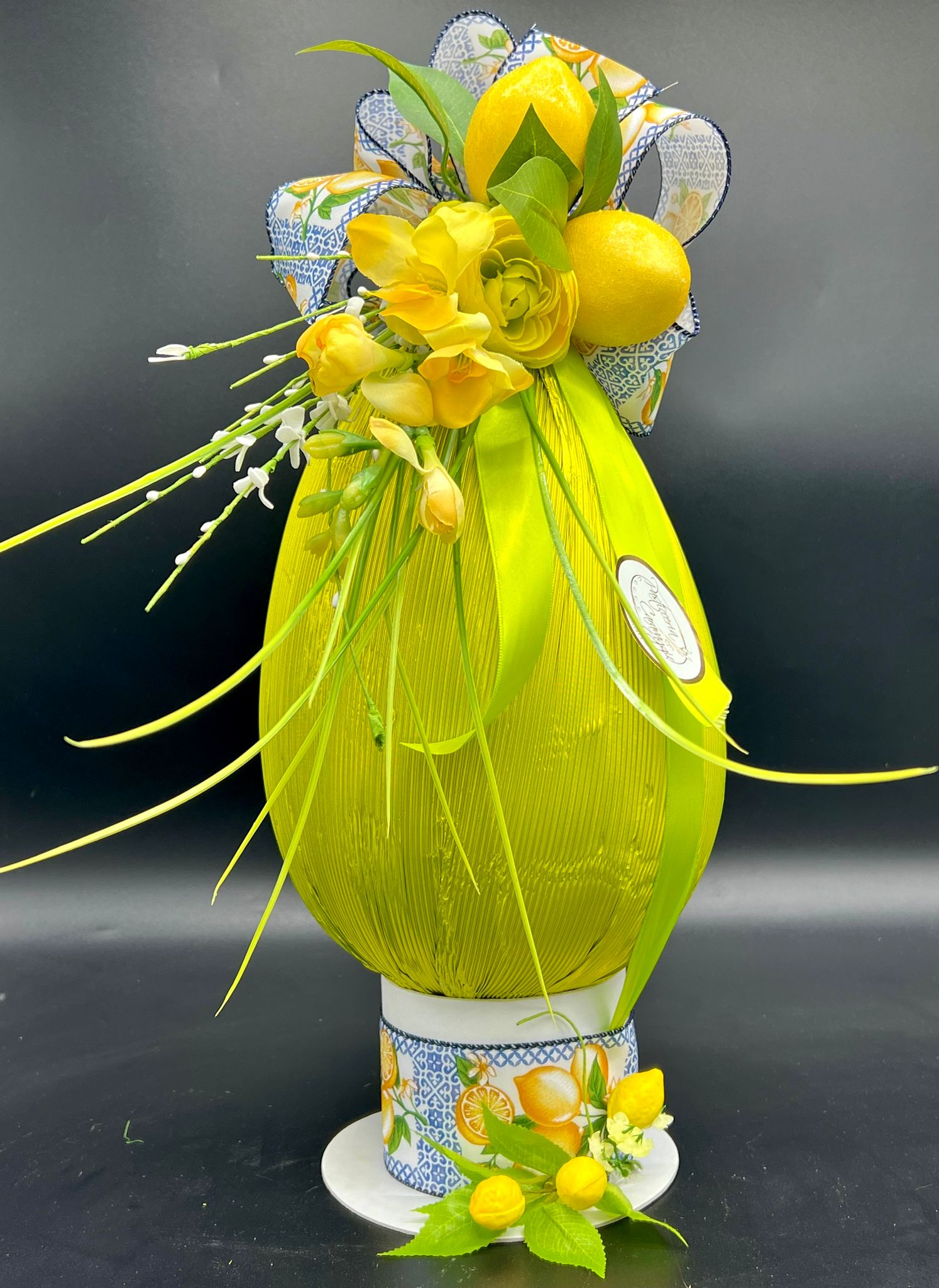 Piccolo uovo di cioccolato fasciato in tessuto verde su base in ceramica con fiori di limone, pasticceria Caravaggio Pasqua 2024