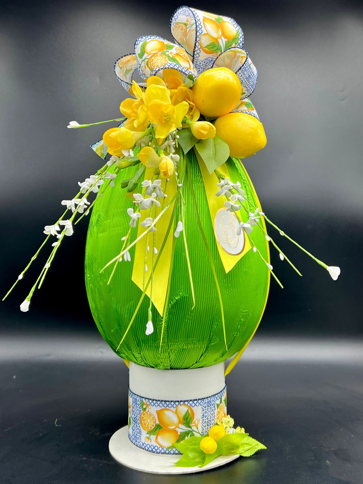 Uovo di cioccolato fasciato in tessuto verde su base in ceramica con fiori di limone, pasticceria Caravaggio Pasqua 2024