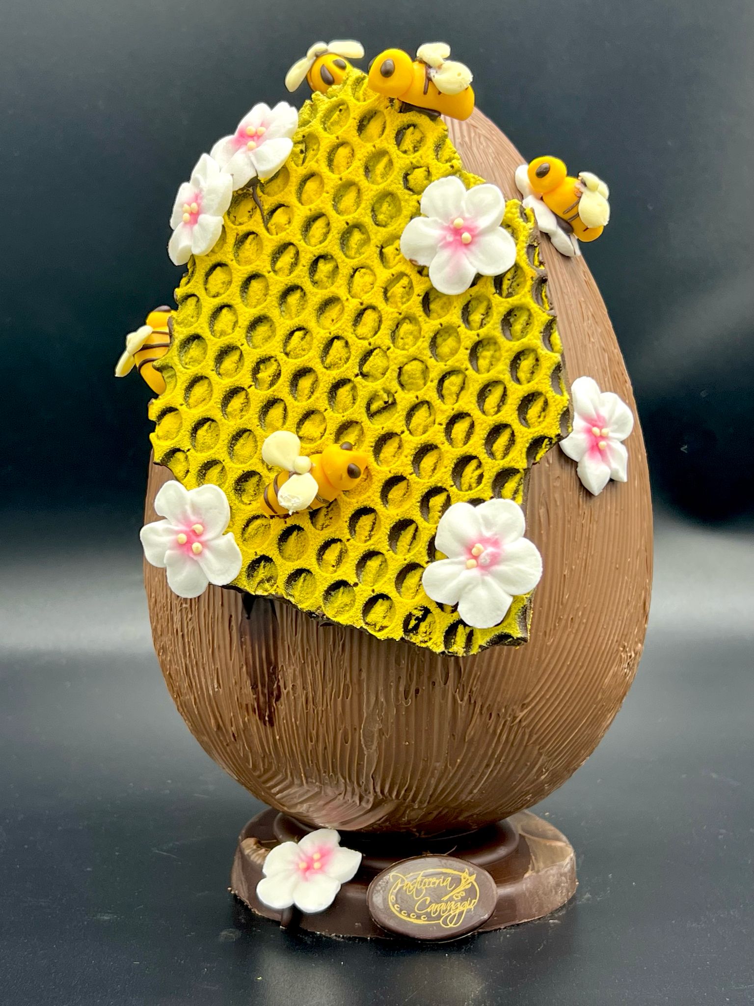 Uovo di cioccolato decorato con nido d'api e fiori di pasticceria Caravaggio, Pasqua 2025