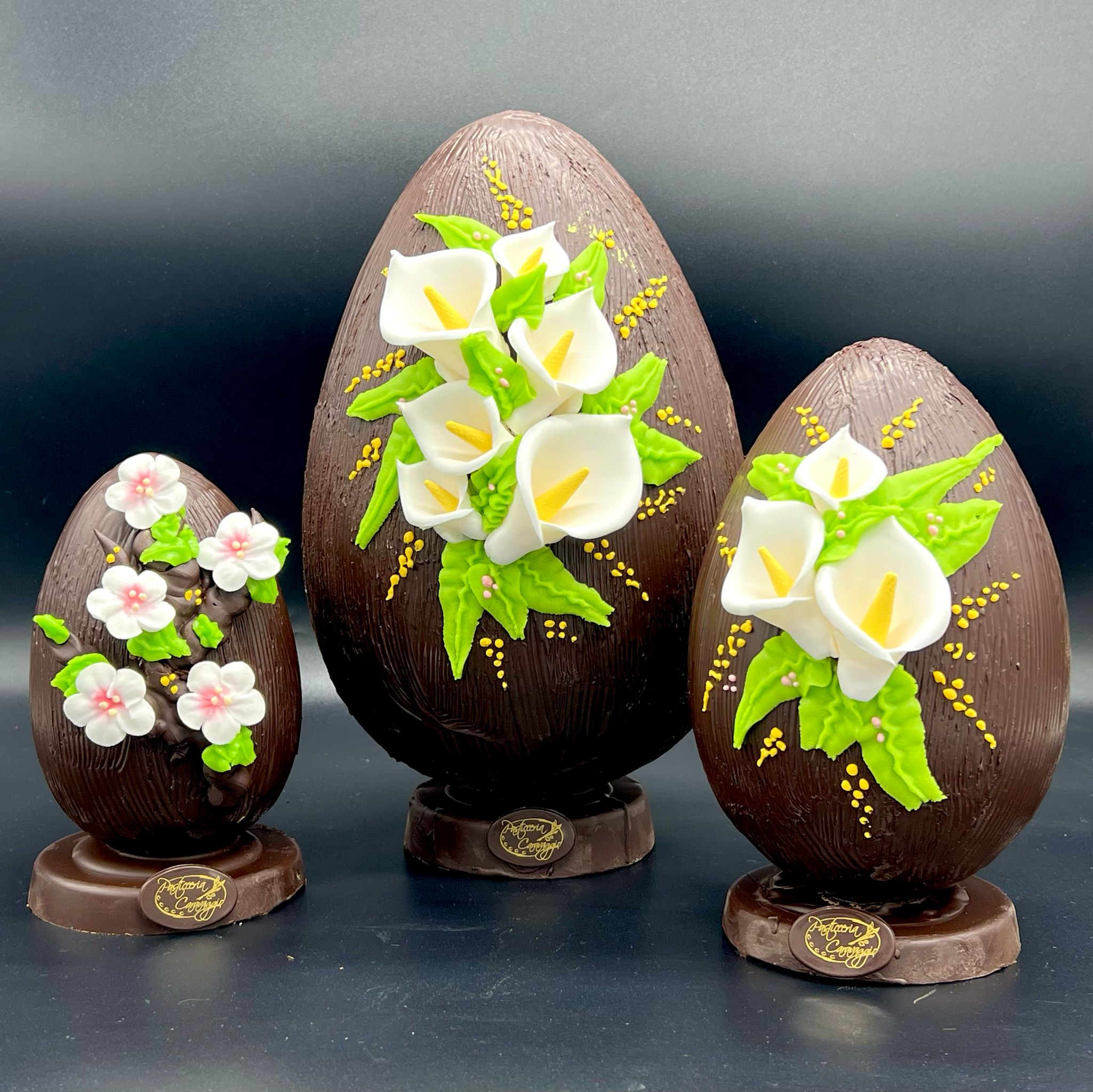 Tre uova di cioccolato fondente decorate con calle e fiori di pesco, pasticceria Caravaggio Pasqua 2025