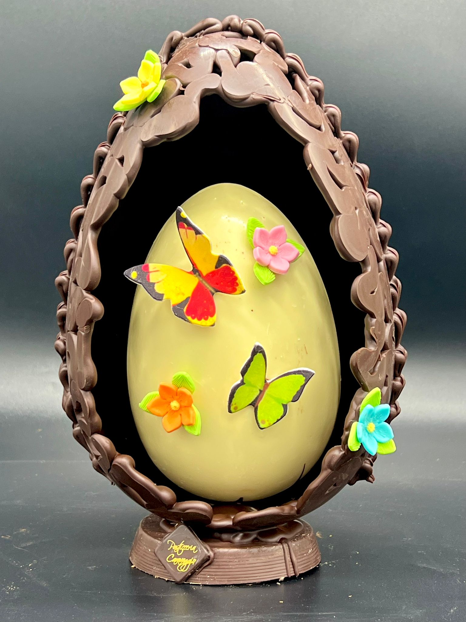 Uovo di cioccolato con farfalle e fiori colorati in un nido di cioccolato fondente