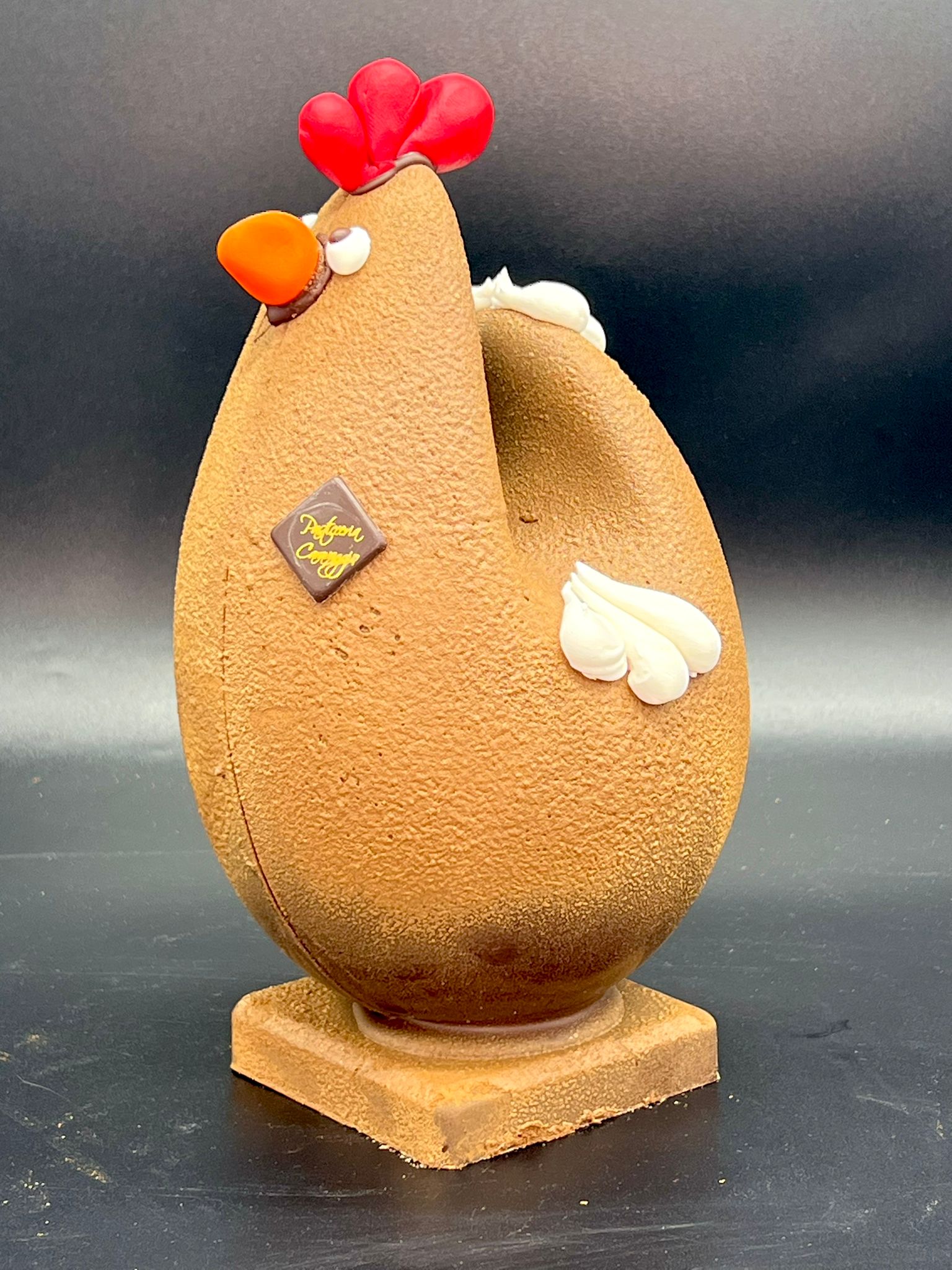 Uovo di cioccolato a forma di gallina con cresta rossa e ciuffi di panna